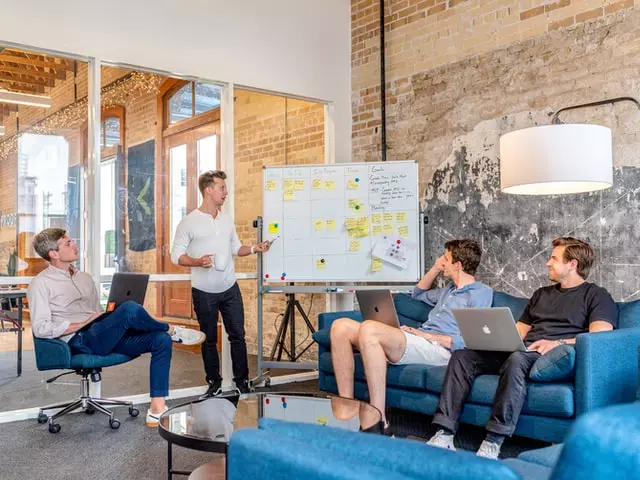 A man in a white t-shirt presenting to a group of 4 in front of a whiteboard